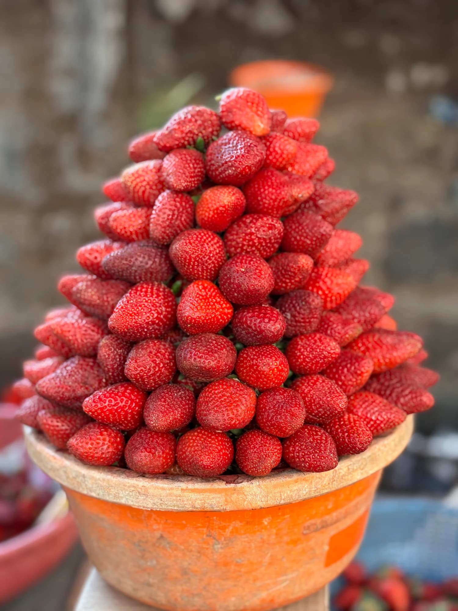 Strawberries piled high in an orange bowl at a market.