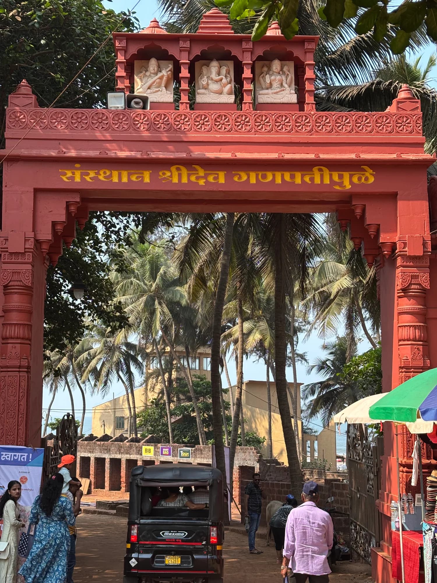 A red temple entrance with palm trees and a street beyond it.