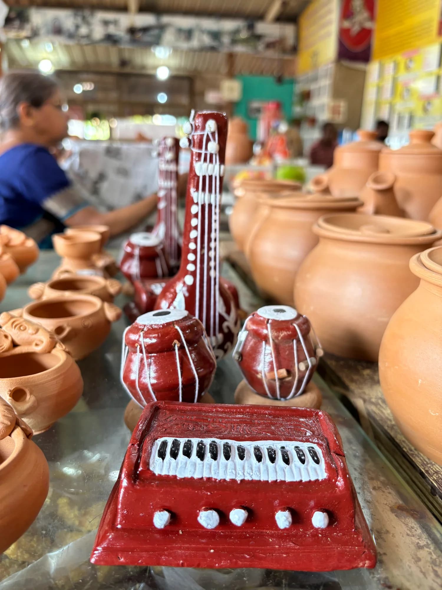 A red ceramic musical-instrument sculpture surrounded by clay pots.