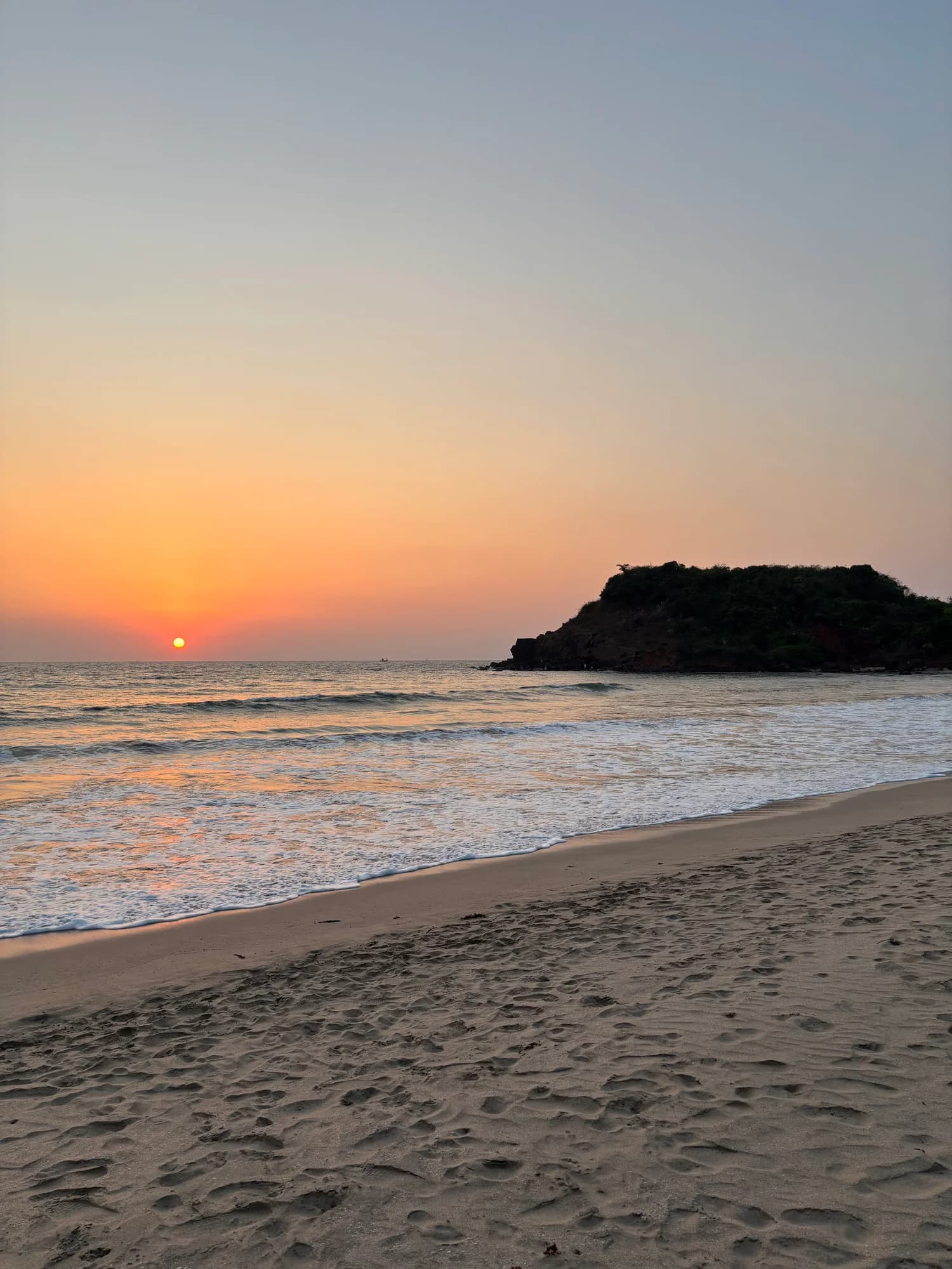 The sun setting over waves and a sandy beach.