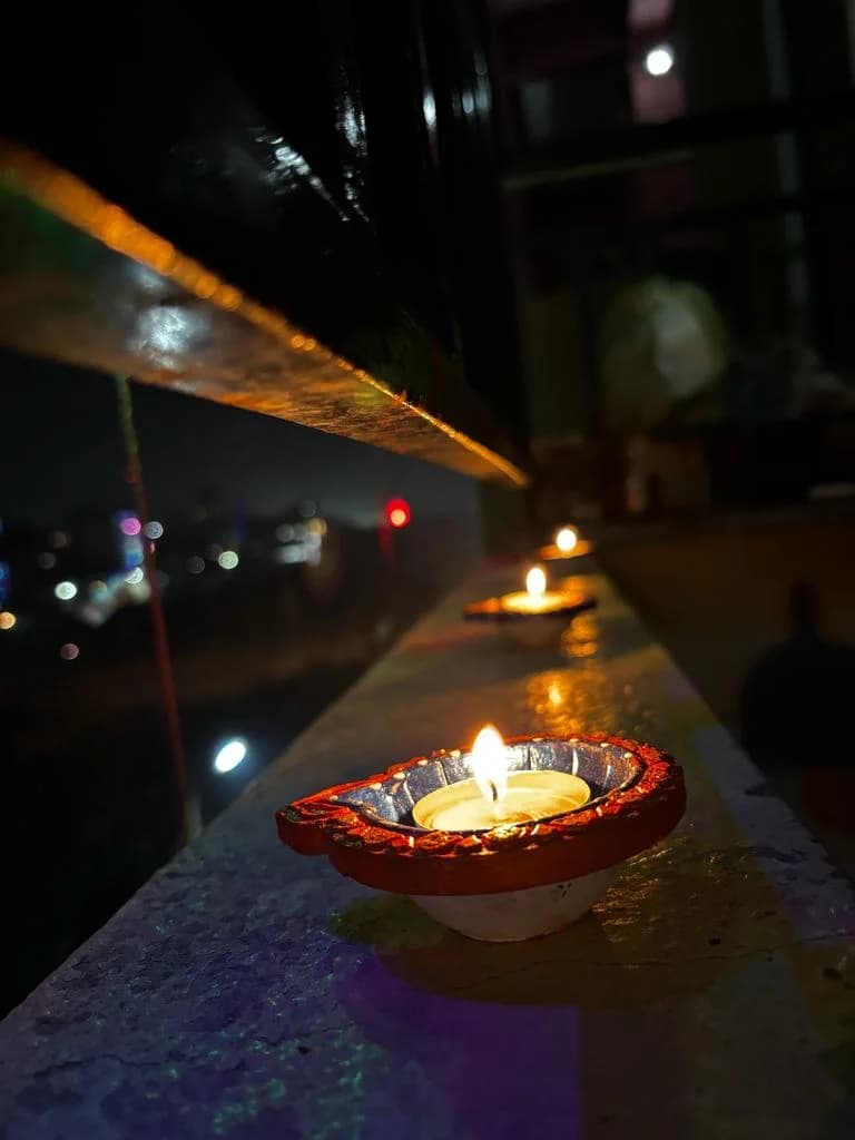 A row of small oil lamps glowing beside a reflective railing at night.