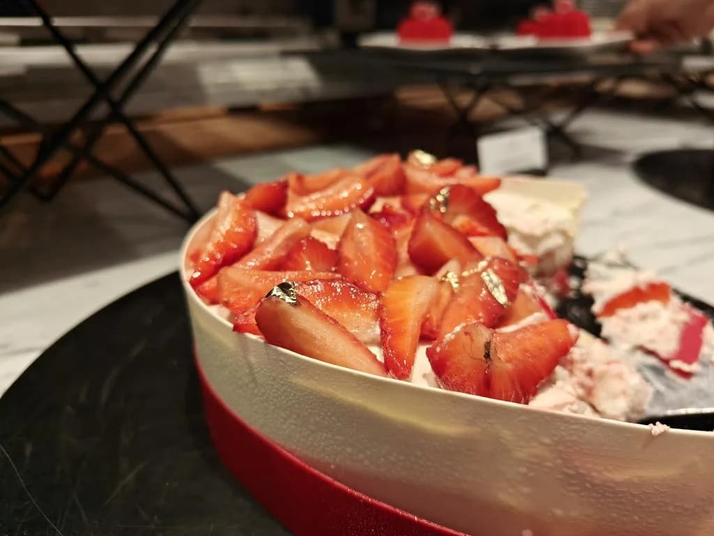 Strawberry pieces piled in a red bowl at a dessert counter.